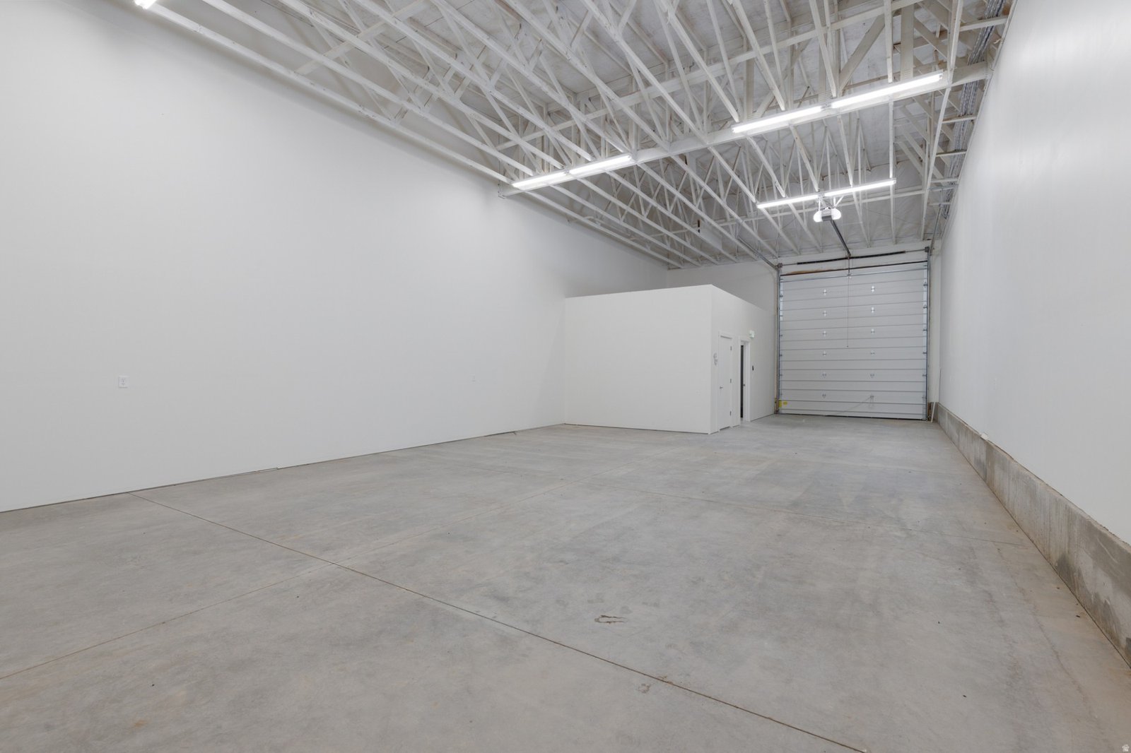 Interior of a Hyrum Flex unit with white walls, a concrete floor, and an overhead door
